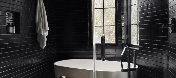 Luxury walk-in shower clad in glossy black tile with a freestanding soaking tub, geometric tile flooring, and black-framed windows.